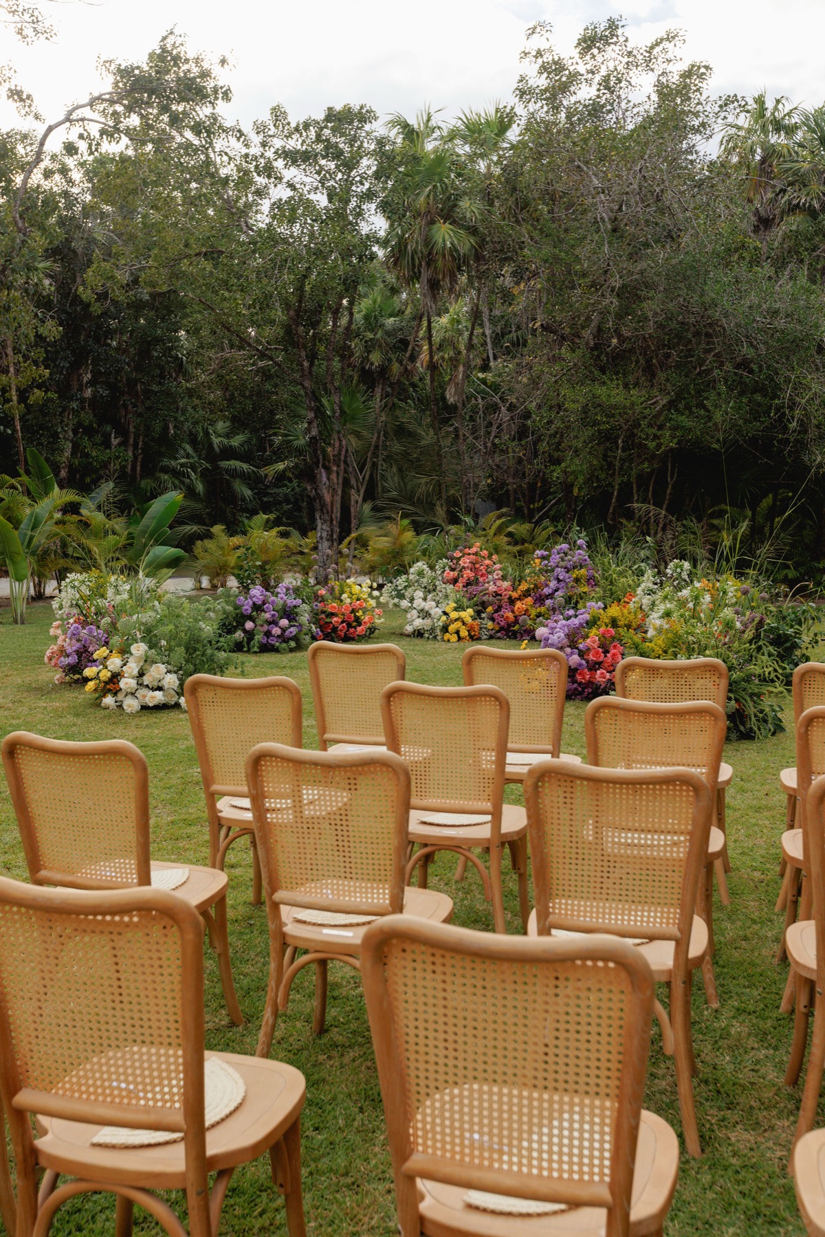 Outdoor ceremony with cane chairs facing a colorful tropical floral altar