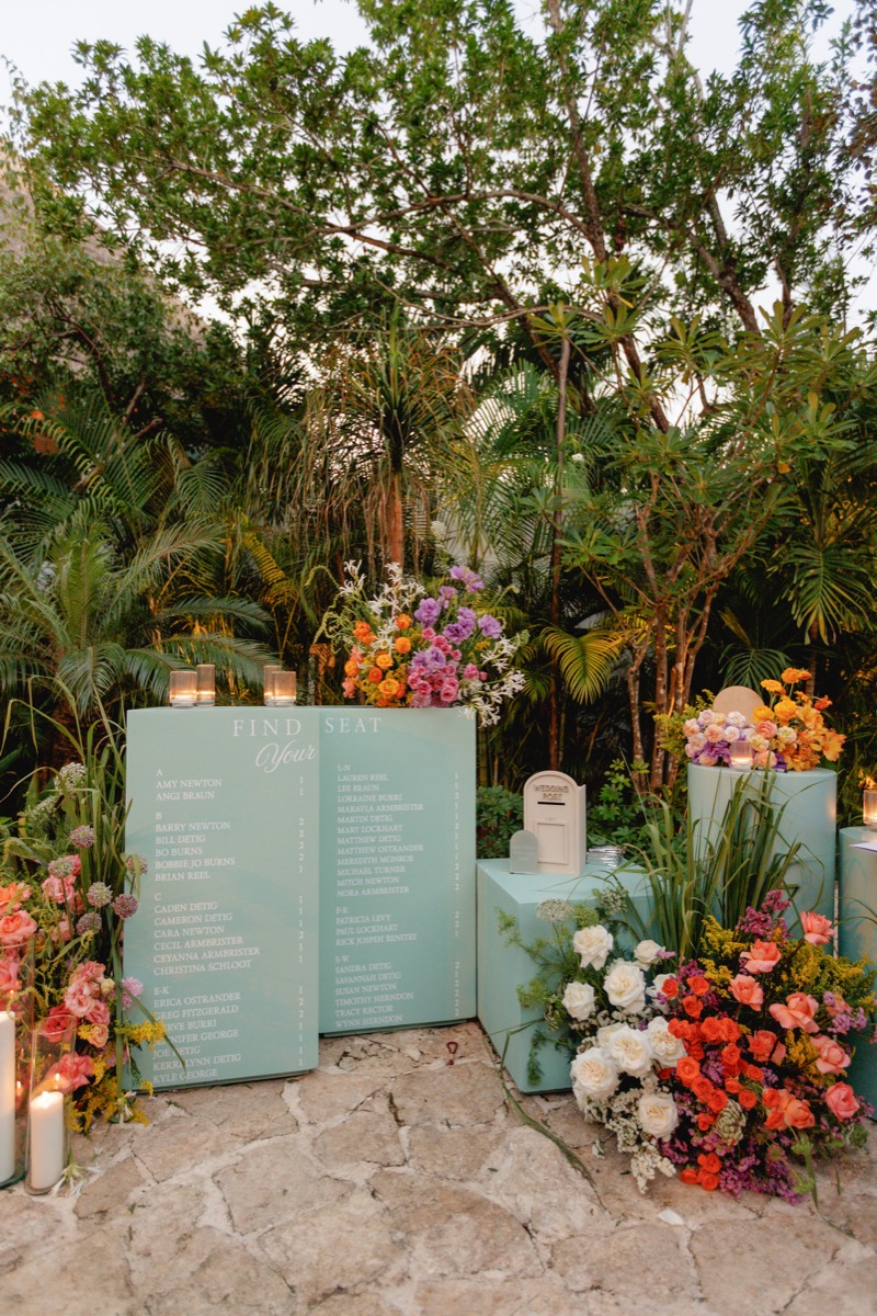 Mint green seating chart flanked by tropical florals and tall palms