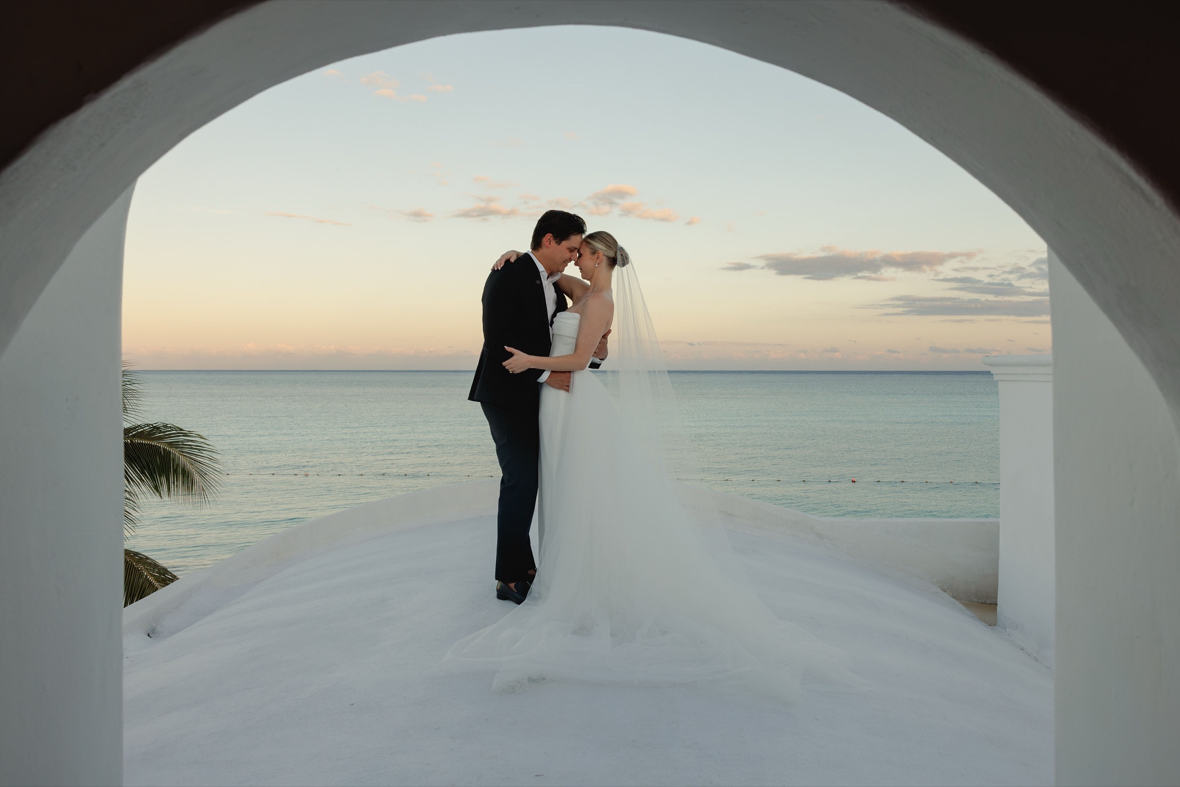 Cara & Joseph — the couple under the seafront arch at sunset, Belmond Maroma