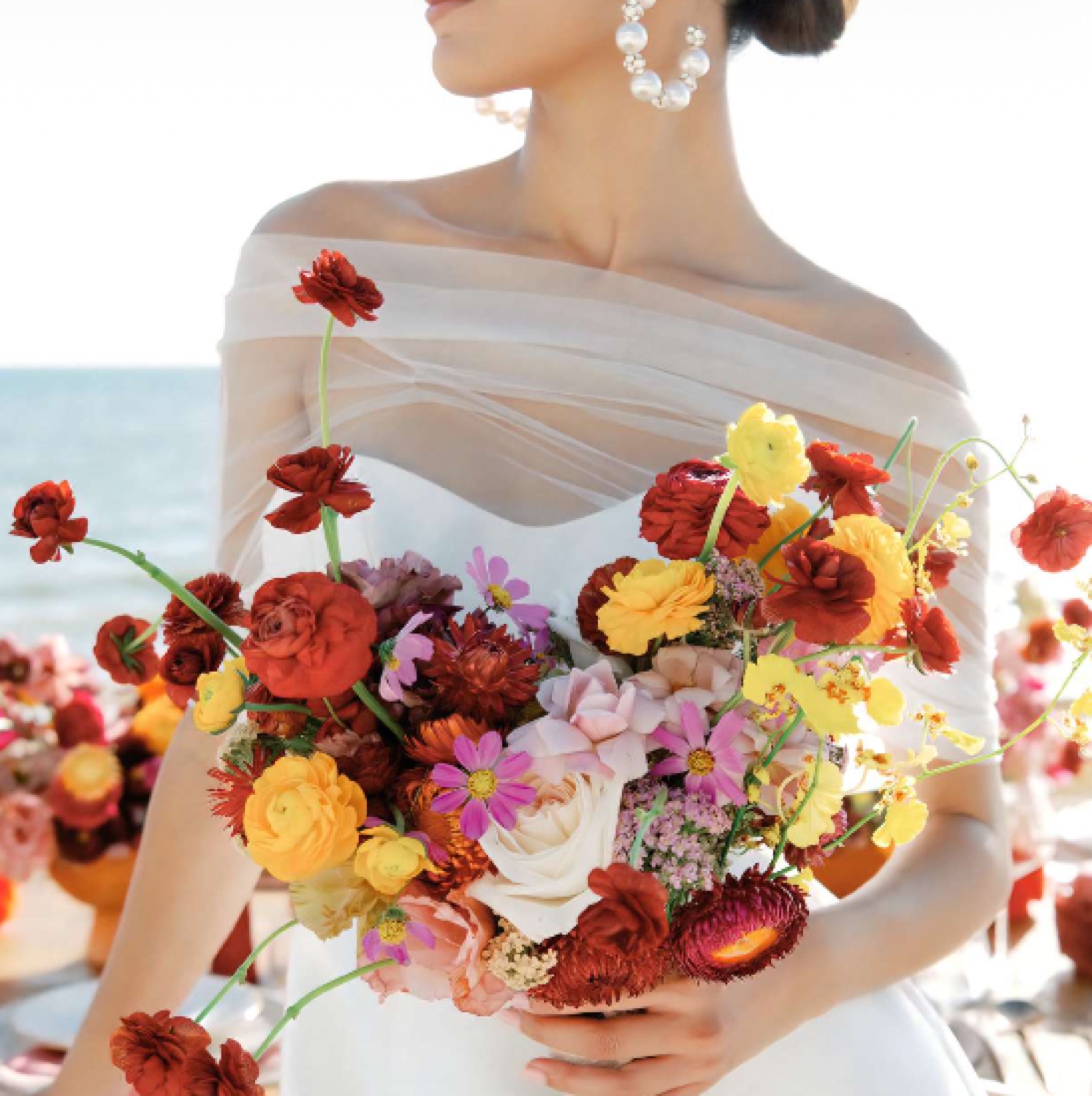 Vibrant bridal bouquet of red, pink and yellow blooms by the ocean