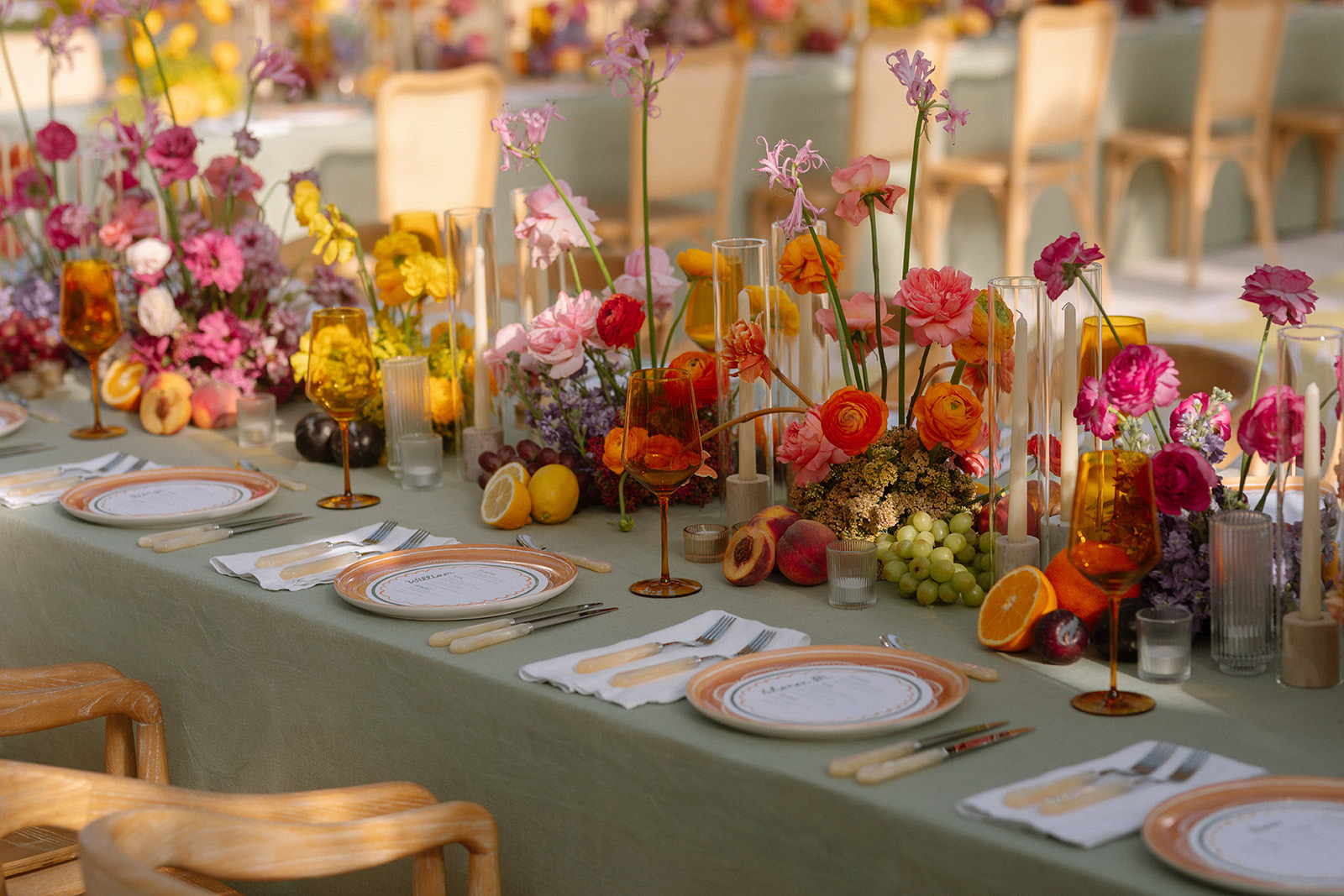 Long reception table dressed in sage linen with abundant fruit, florals and amber glassware