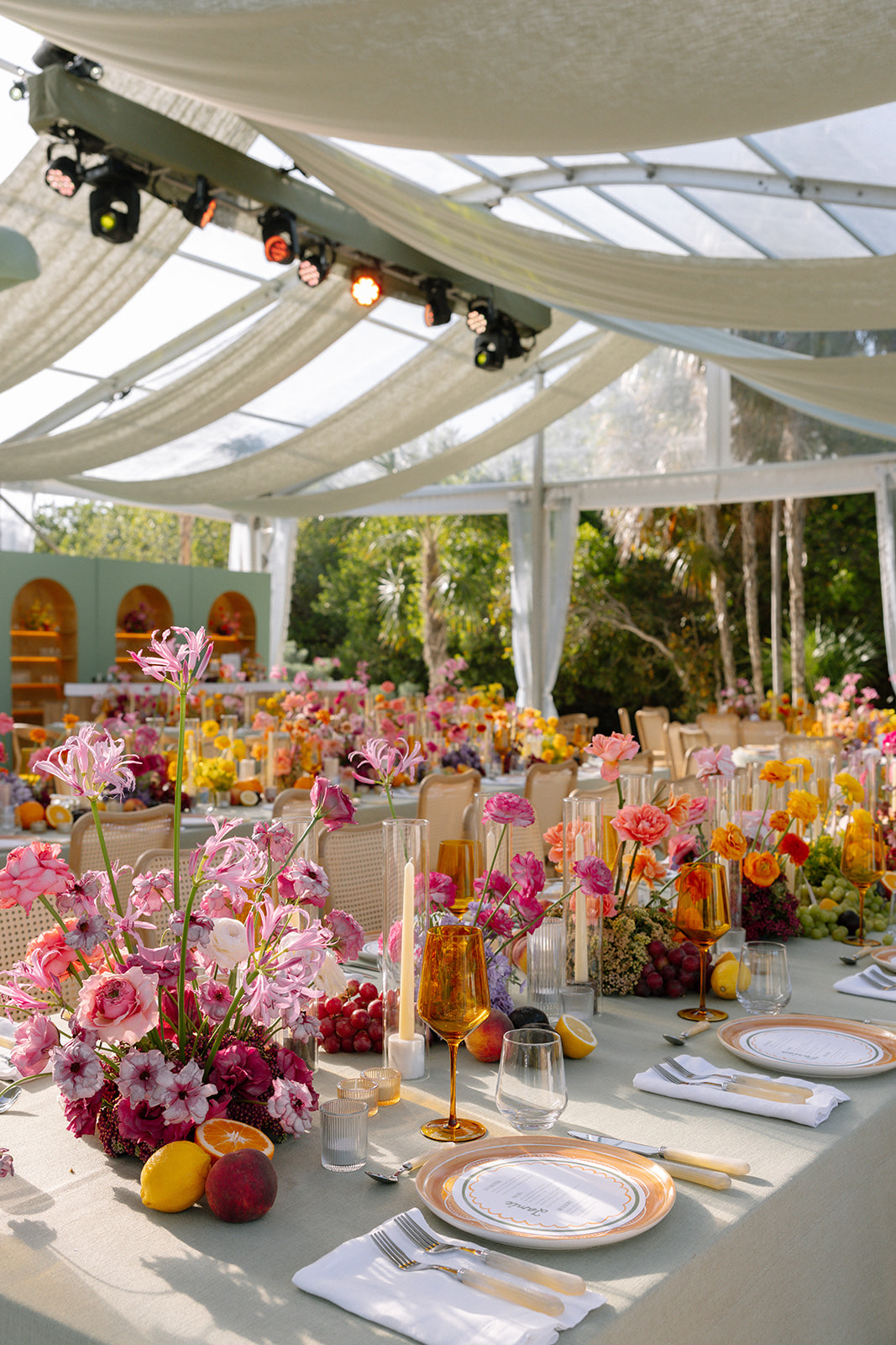 Wide view of the reception under draped fabric, sage tables with abundant pink and yellow florals