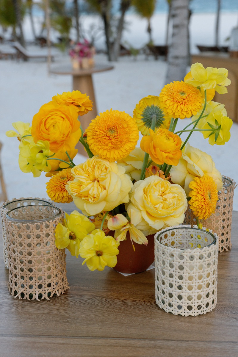 Yellow ranunculus and rose centerpiece flanked by woven votive holders