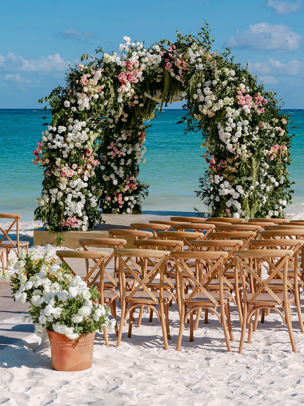 Open-air beach floral arch with cascading white, blush and pink blooms framing a ceremony aisle