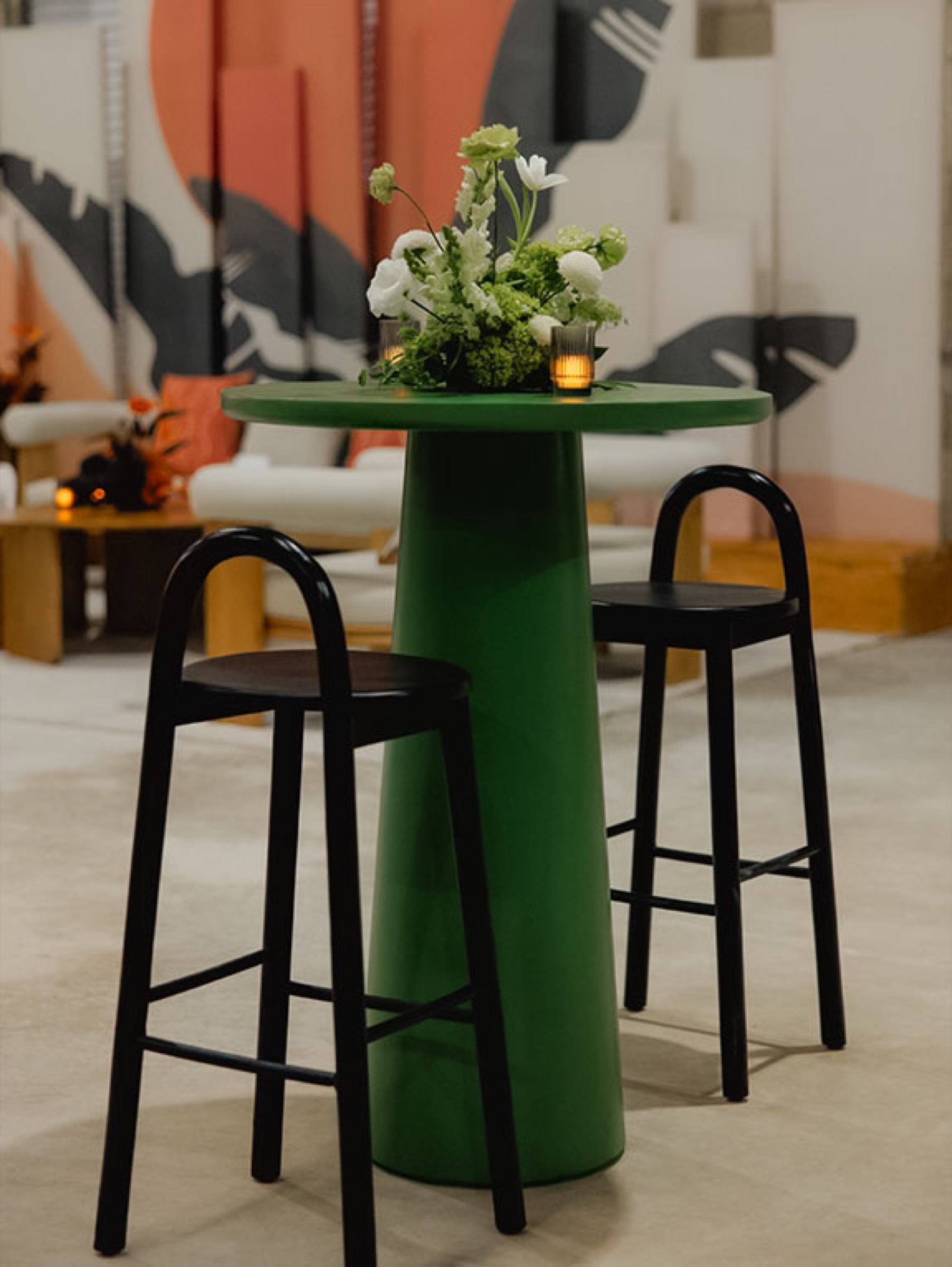 Emerald green high-top table with black bar stools and a green-and-white floral arrangement