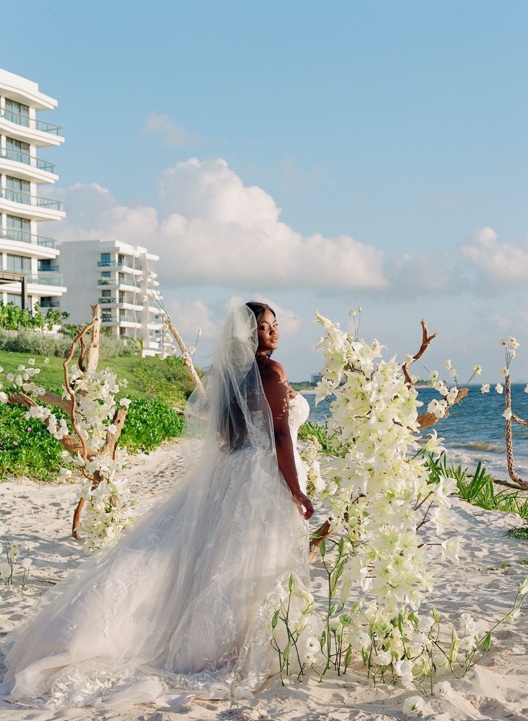 Bride beside lush white floral driftwood installations on the beach