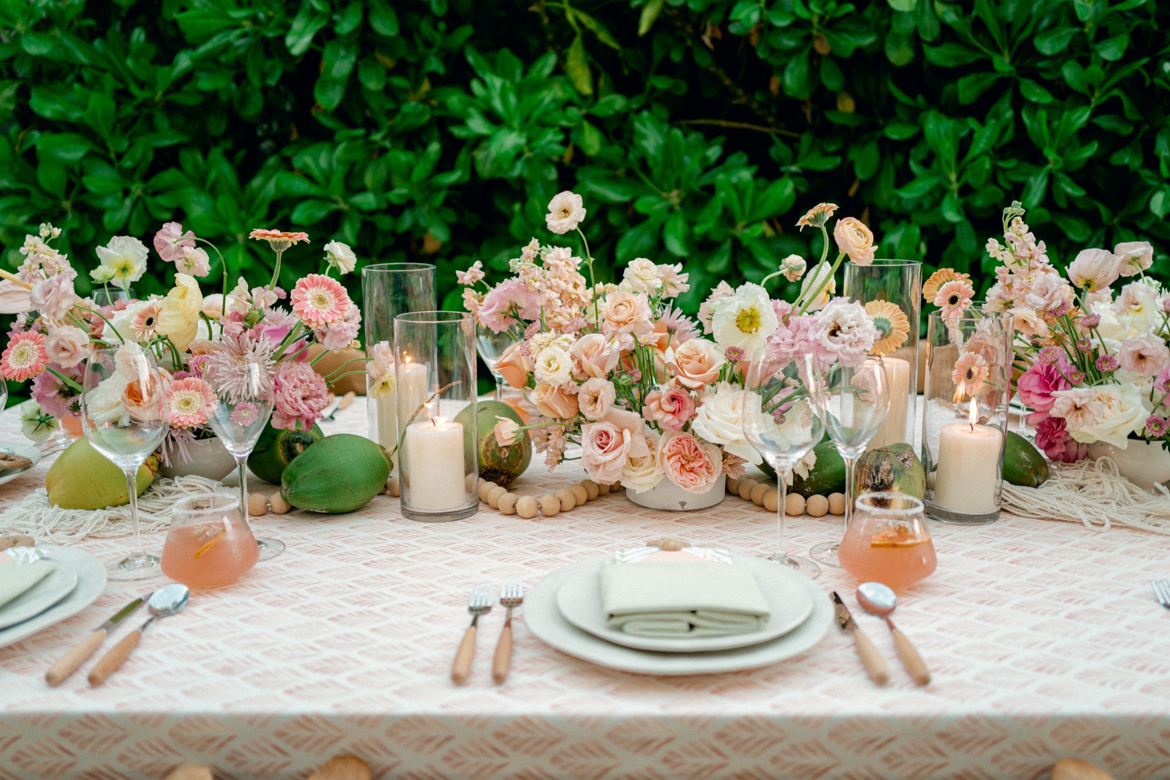 Canteiro tablescape with peach and blush florals against a tropical green hedge