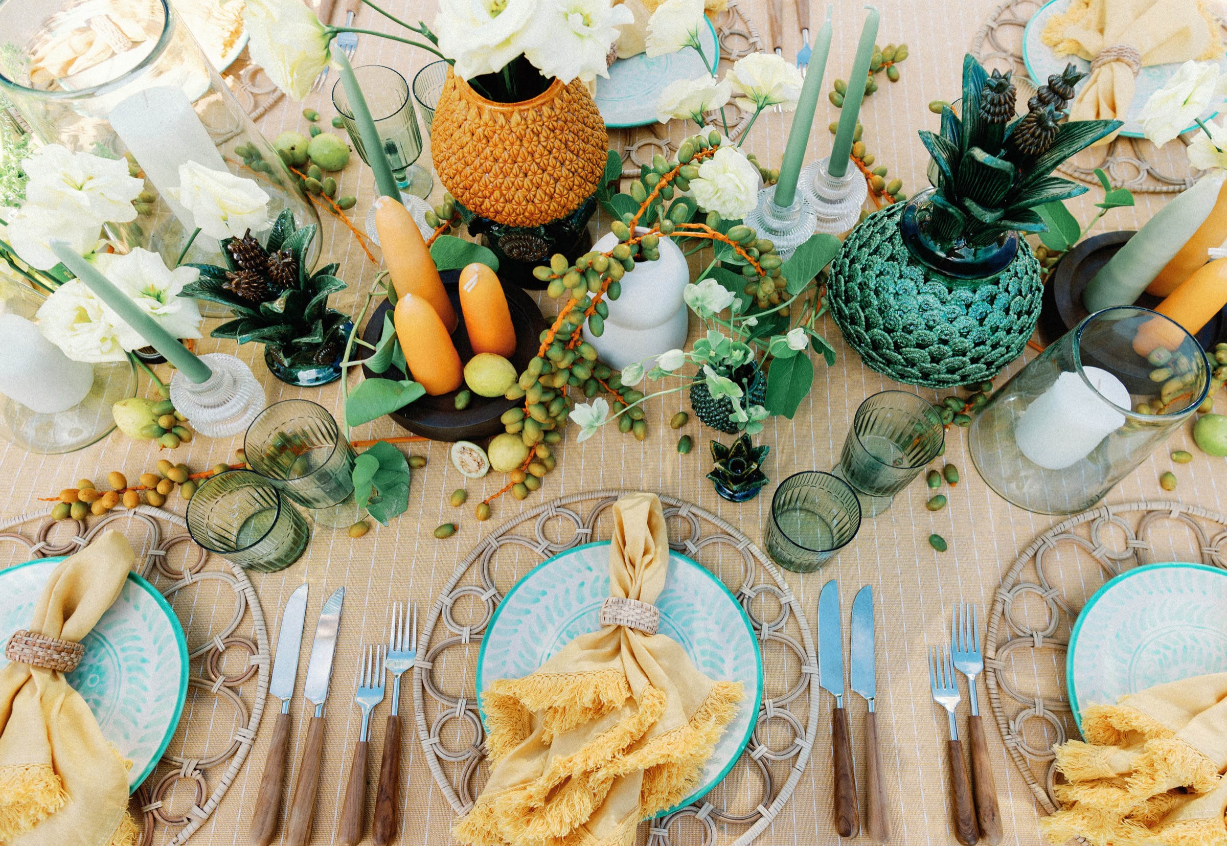 An editorial Canteiro tablescape — turquoise plates, golden linen napkins, tropical centerpieces and green glassware